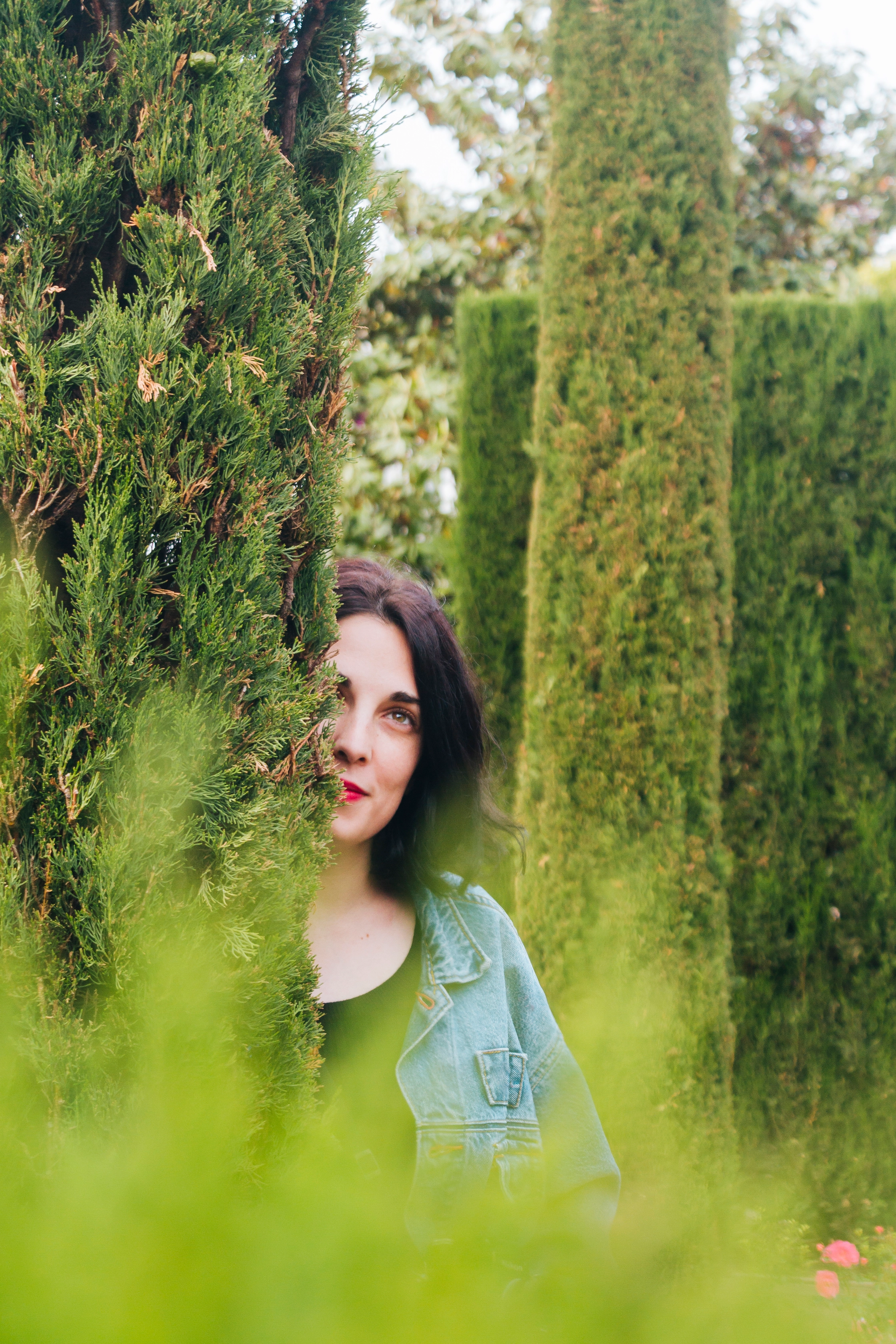 day-dreaming-young-woman-peeking-through-hedge
