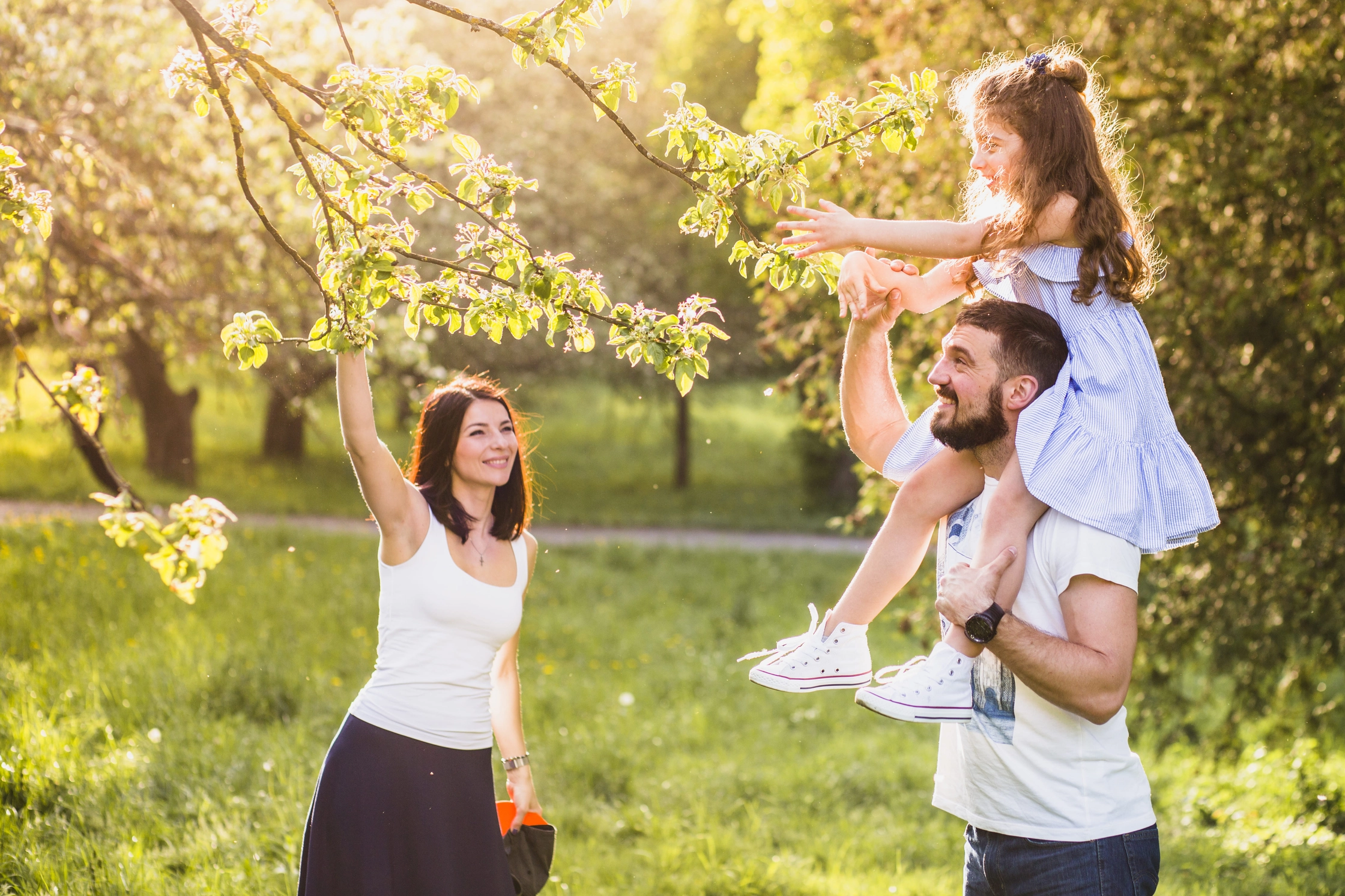 girl-sitting-her-father-s-shoulder-picking-tree-leaf-with-mother