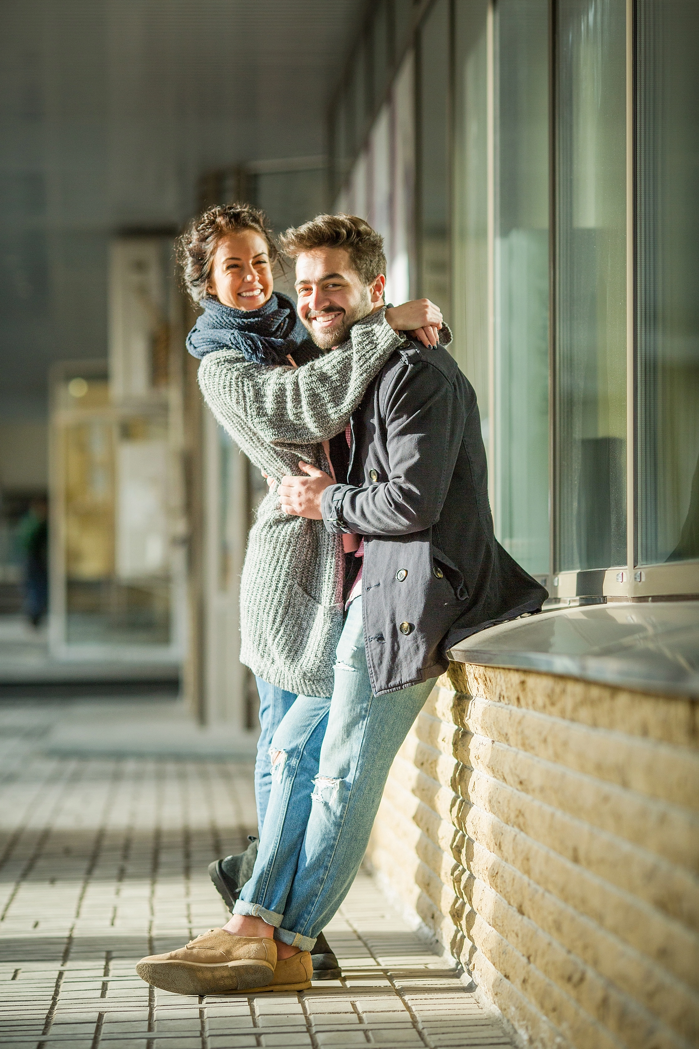 happy-couple-hugging-outdoors-handsome-man-holding-his-girl-friend-looking-camera-near-business-centre