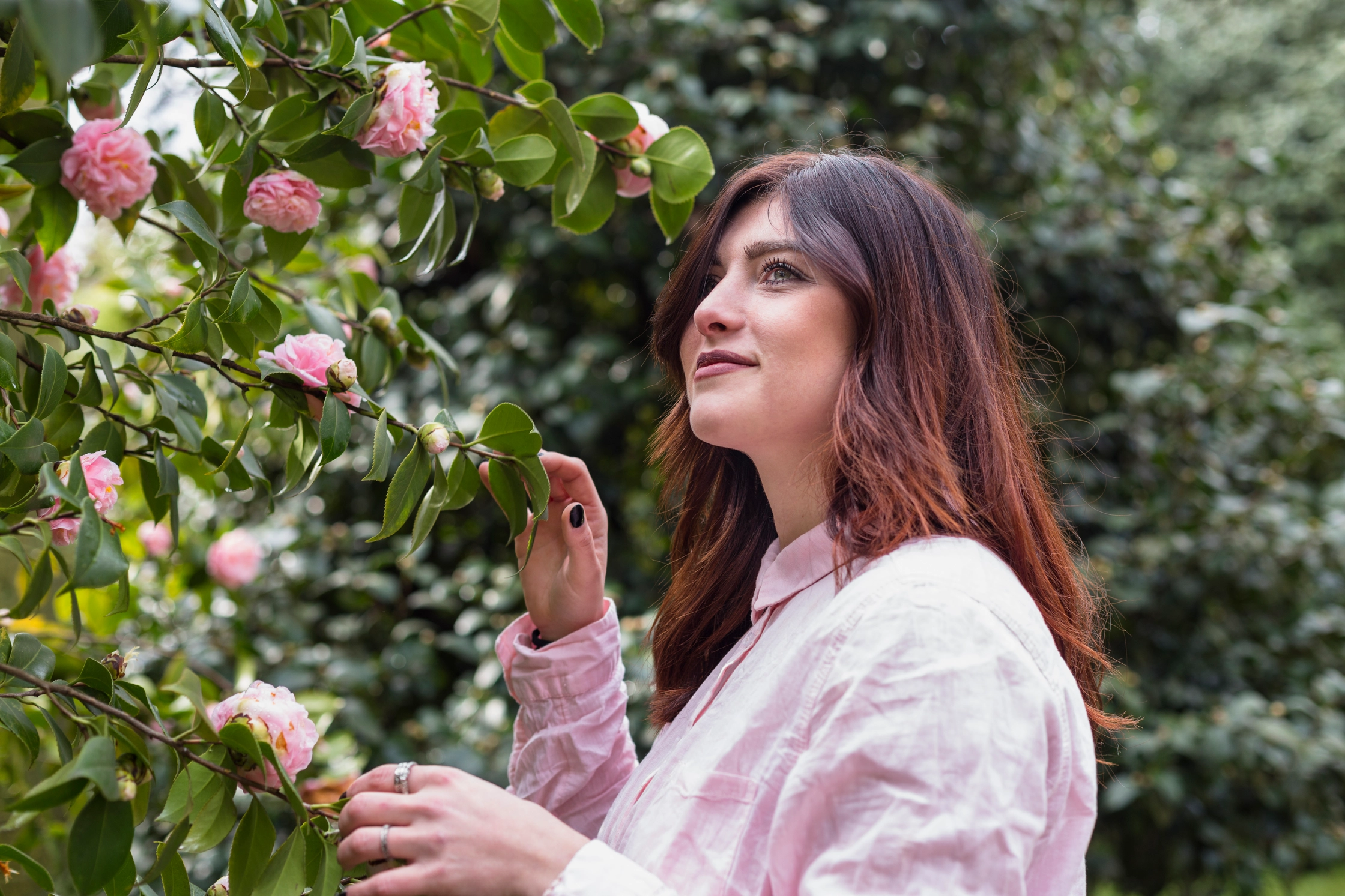 positive-woman-near-pink-flowers-growing-green-twigs