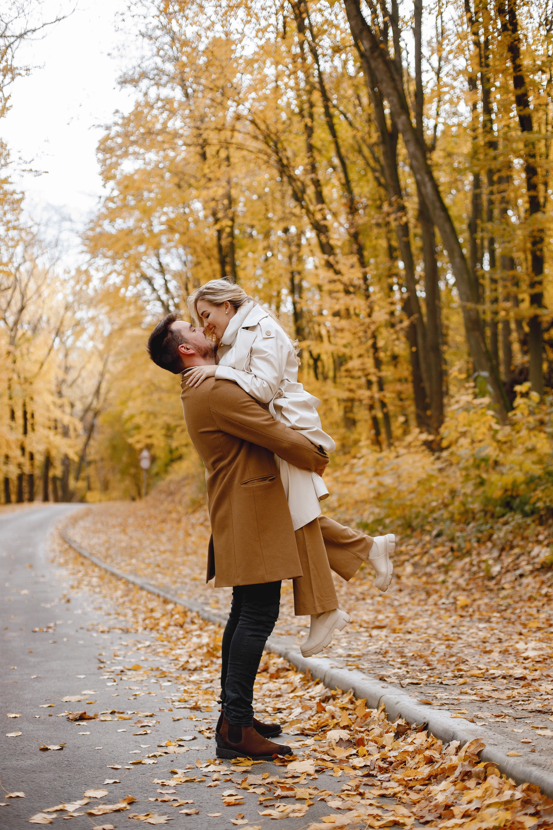 young-man-woman-walking-outside-wearing-beige-coats-blond-woman-brunette-man-autumn-forest-romantic-couple-kissing